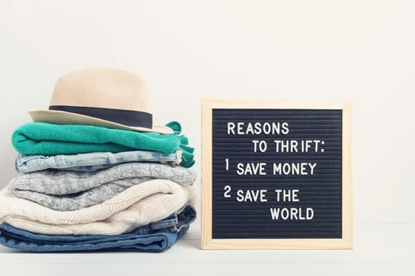 A pile of second hand clothes and a sign describing reasons to shop in second hand stores
